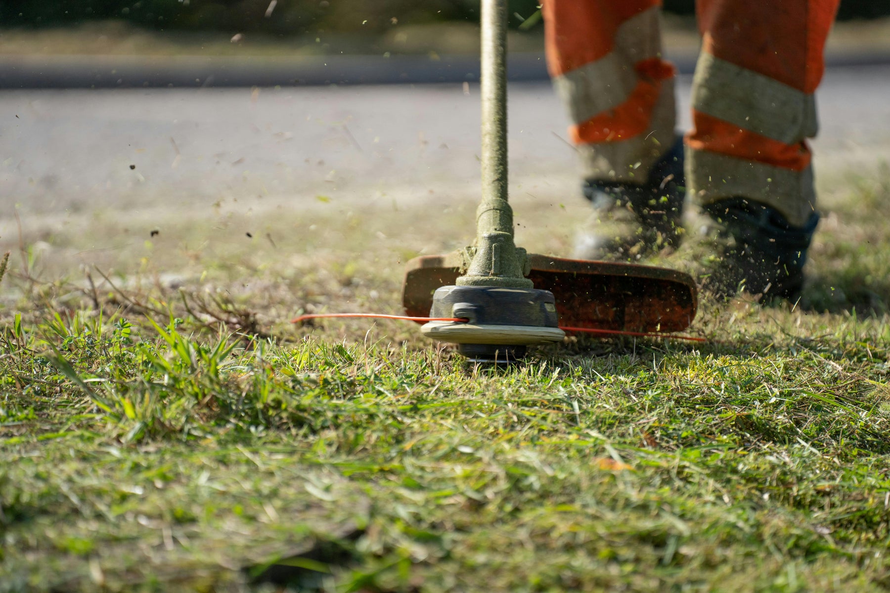 A weed trimmer cutting grass and weeds along a road