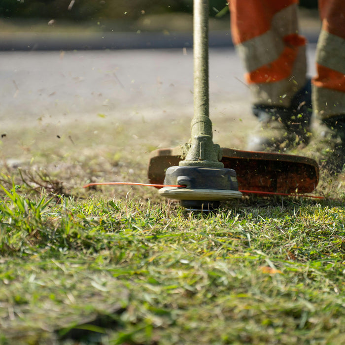 A weed trimmer cutting grass and weeds along a road