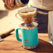 Person pouring coffee into a Dometic cup on a wooden surface.