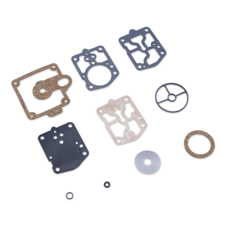 A set of flat mechanical gaskets, seals, and rings laid out on a plain white background. The pieces include several dark gray rubber gaskets, one tan gasket, one light beige gasket, a tan ring, a gray circular piece, a translucent white disc, and two small black O-rings.