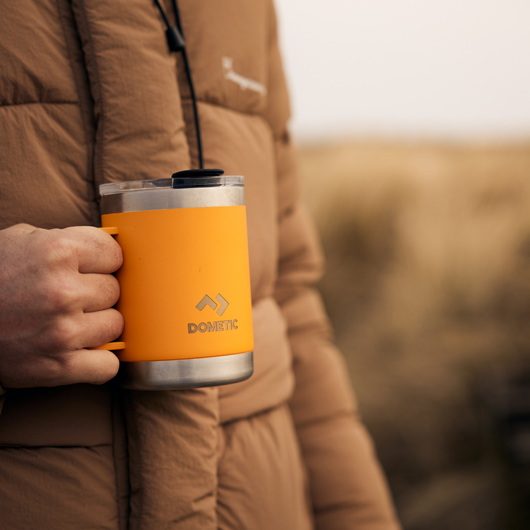Person holding an orange Dometic mug with a blurred natural background