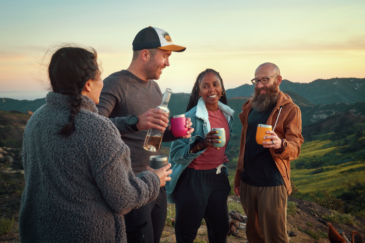 Four people enjoying drinks together on a mountain at sunset