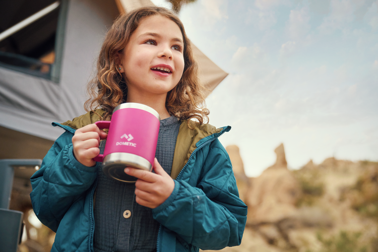 Child holding a pink mug with a scenic outdoor background