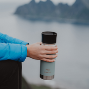Person holding a Dometic brand tumbler with a mountain and lake in the background