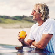 Man holding a yellow mug by a lake with mountains in the background