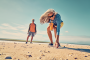 Woman on a beach bending over, man standing in the background