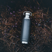 Black water bottle with silver cap on grass and small flowers