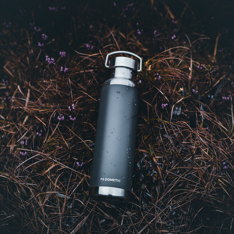 Black water bottle with silver cap on grass and small flowers
