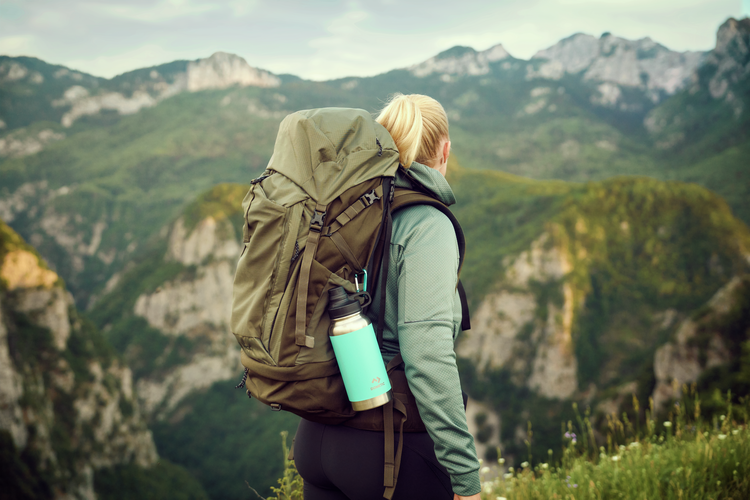 Person with a large backpack and water bottle standing on a mountain top