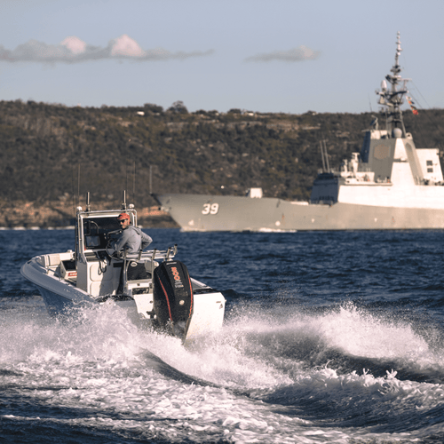 A center console boat with a Mercury engine running across open water near a military boat