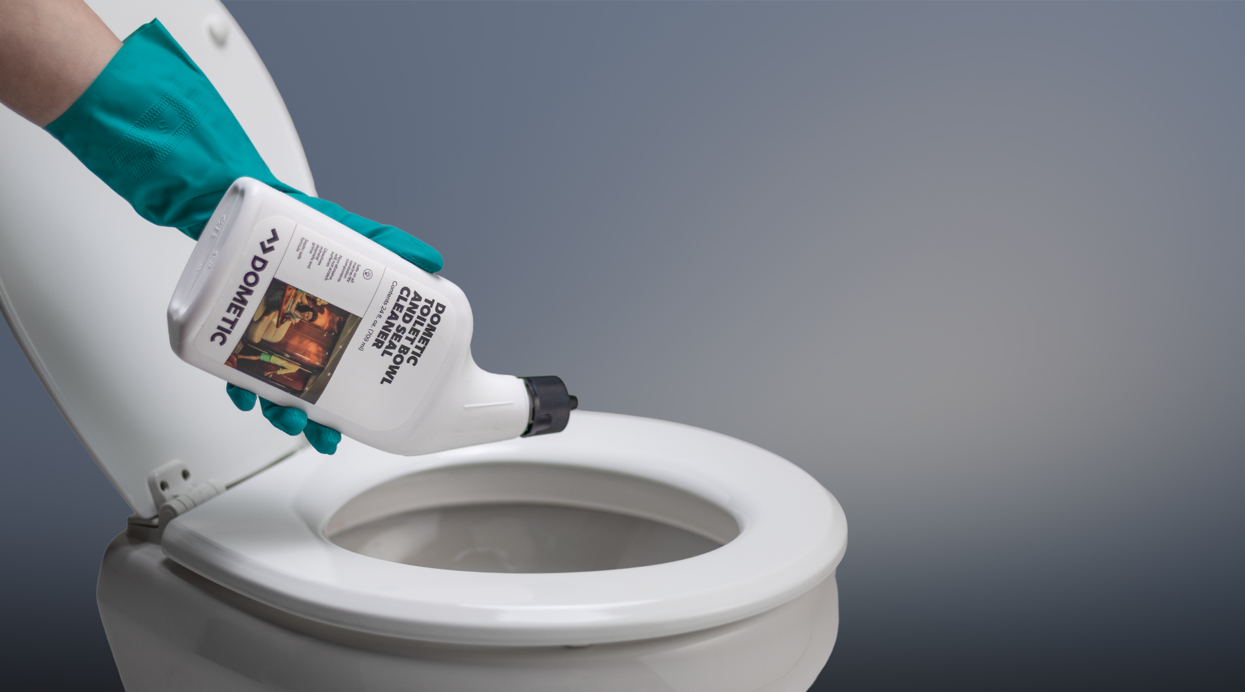 Person with green rubber gloves using a bottle of Dometic toilet bowl cleaner on a toilet with a gray background
