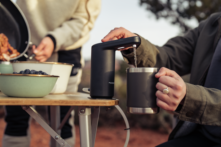 Person pouring coffee from a portable coffee maker into a mug outdoors.