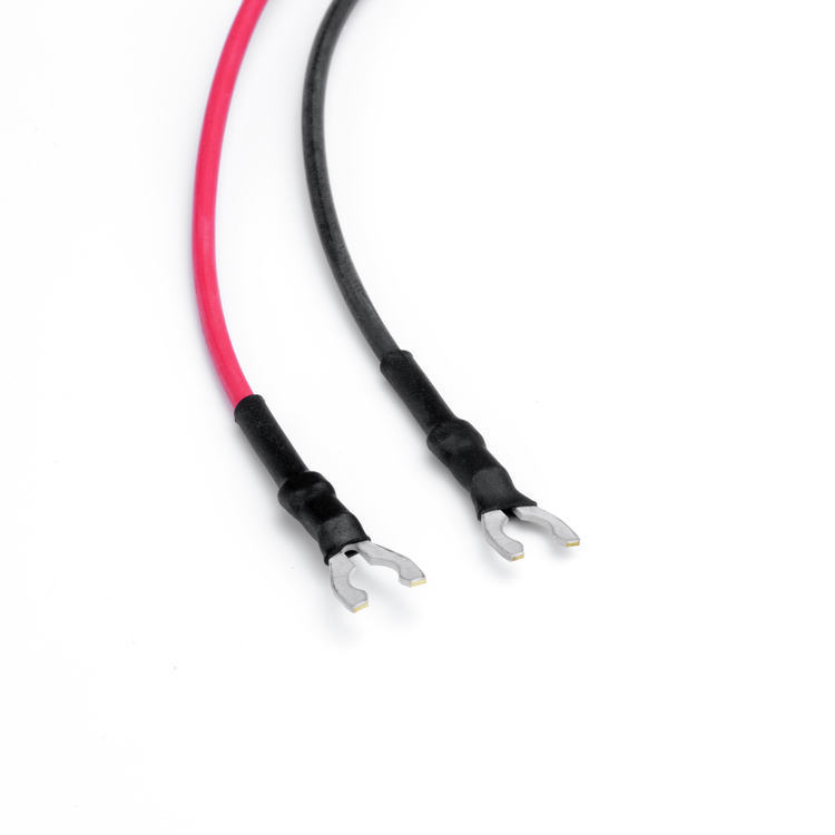 A pair of bare cable leads with red and black insulation, black heat-shrink tubing, and silver metal spade terminals on a white background.