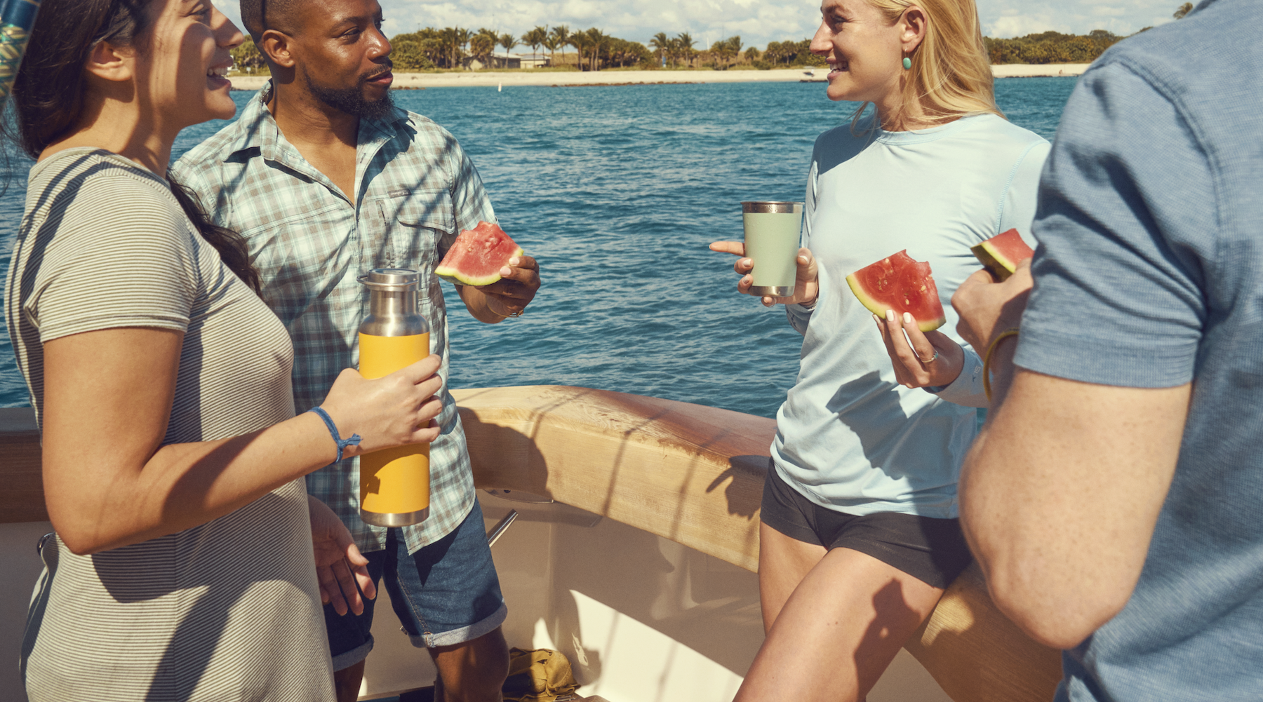 Group of people enjoying drinks and watermelon on a boat with a scenic background.