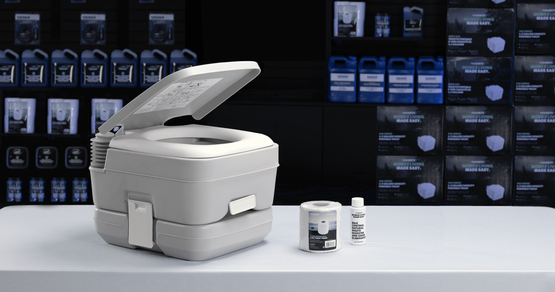 A Dometic 962 series portable toilet, tank treatment, and toilet paper on a shop table.