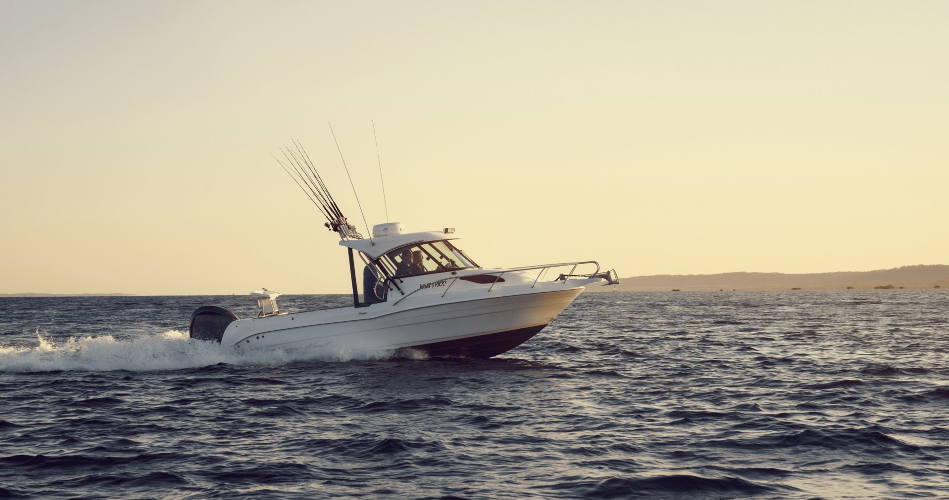A white outboard fishing boat moving across the open water at sunrise