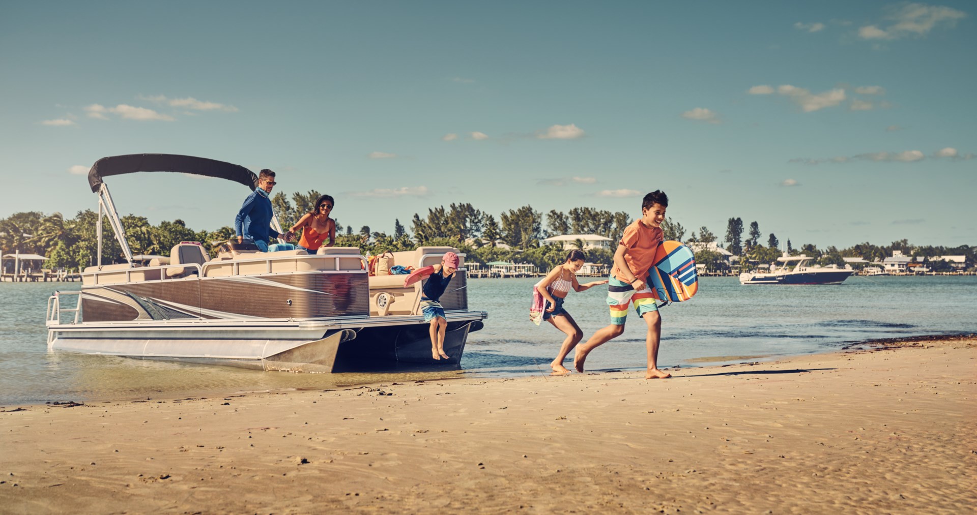 A family of 5 climbing off a pontoon boat that's pulled up on a sandy beach