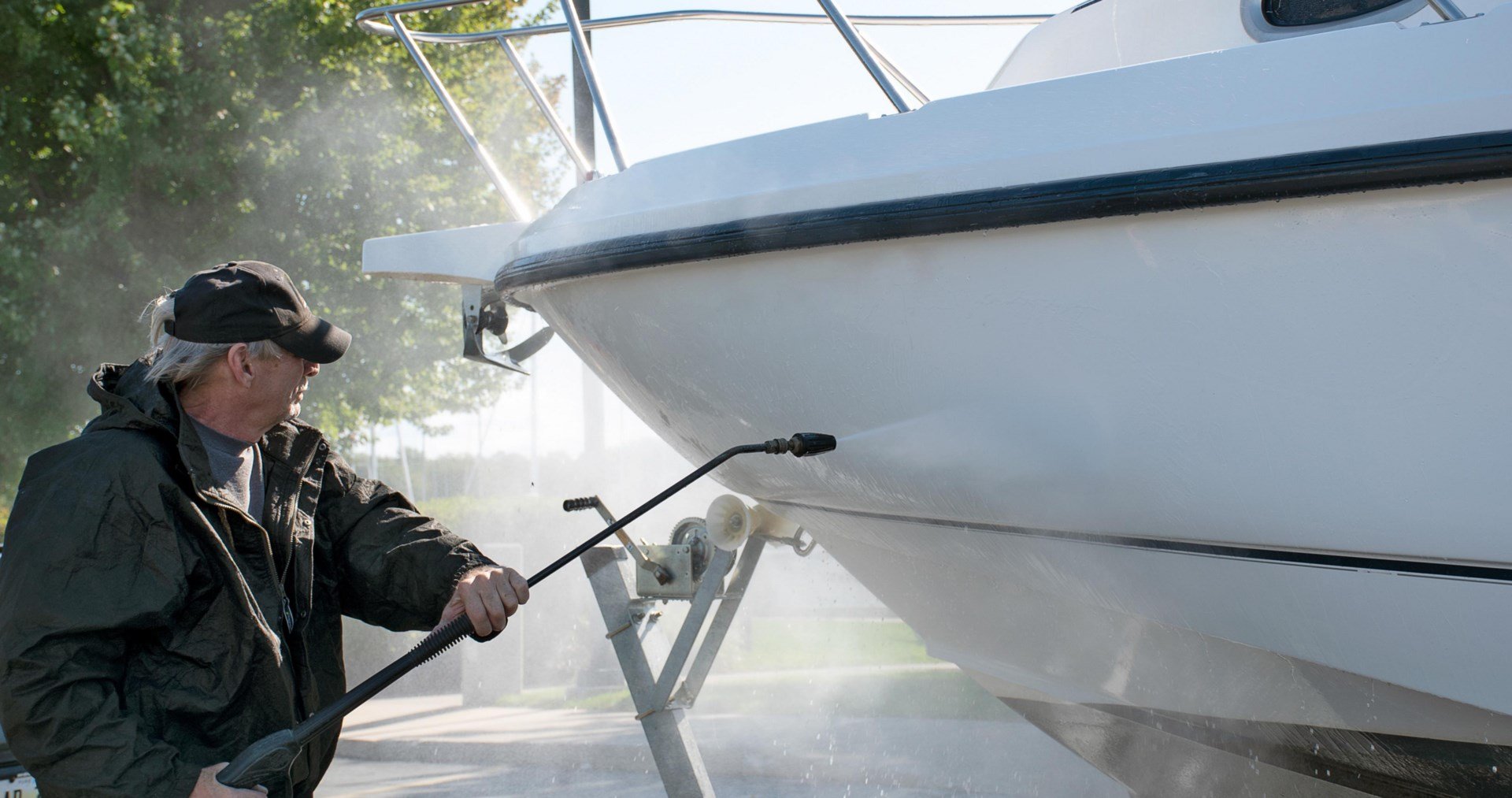 A man using a pressure water to clean a white boat