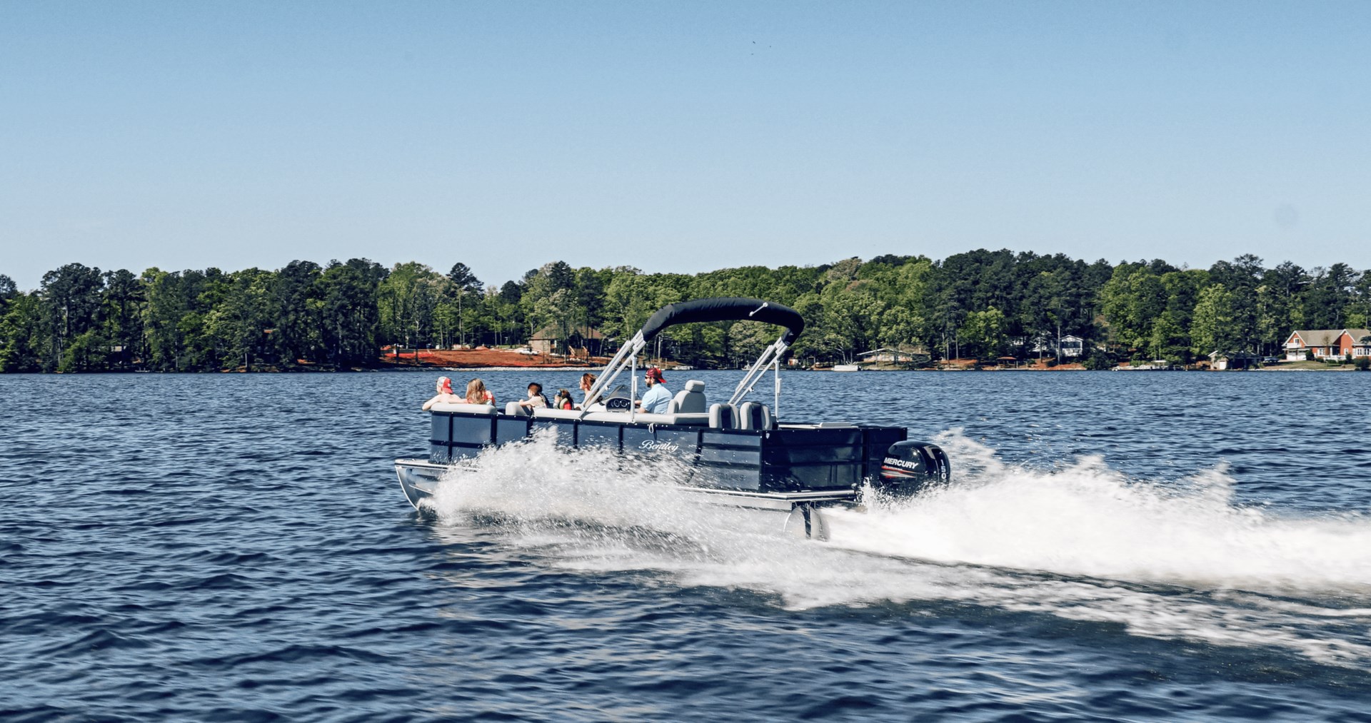 A pontoon boat with several passengers moving across a lake