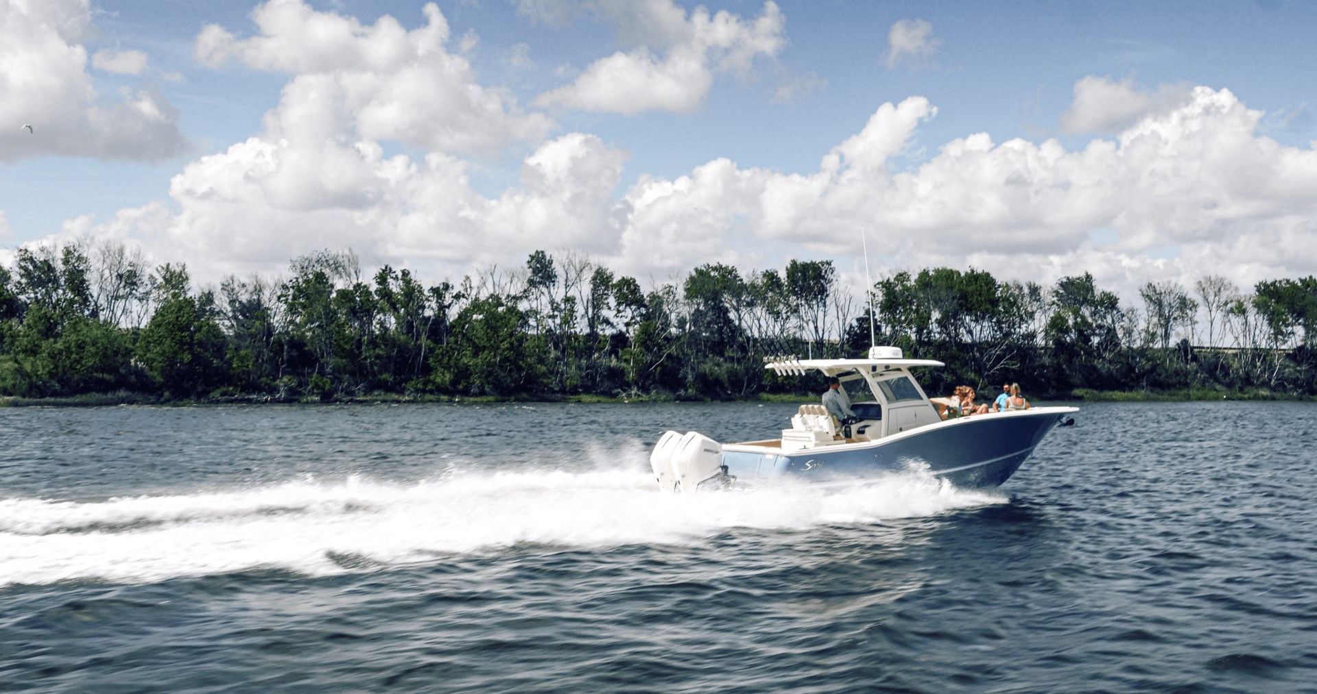 A blue and white center console boat moving quickly on plane along a treed shoreline